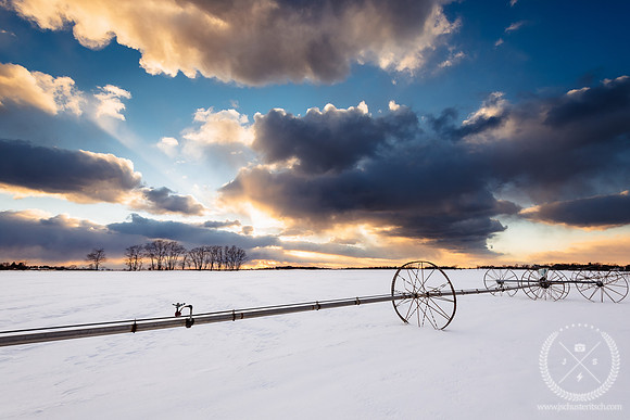 Cloudy Sunset over a Snowy Farm Field